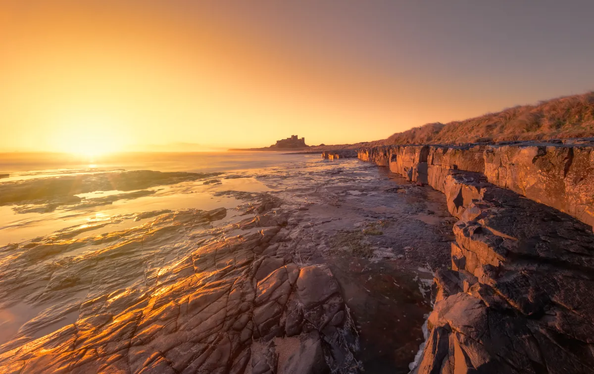 The sun rising over the rocky shore with Bamburgh Castle on the skyline, Northumberland