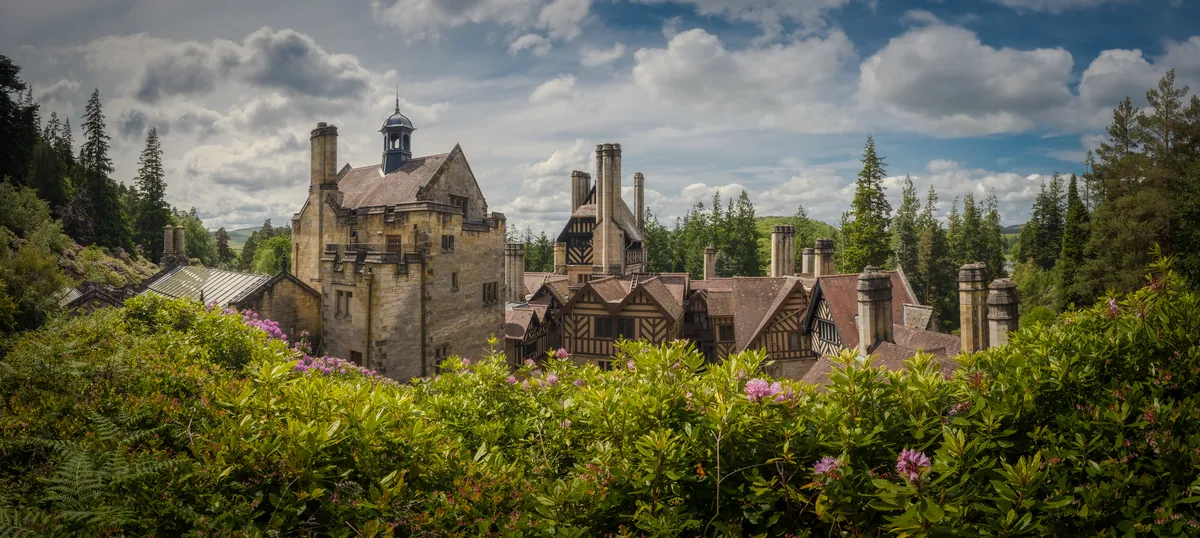 The roofs and chimneys of Cragside above rhododendrons and pines, Northumberland