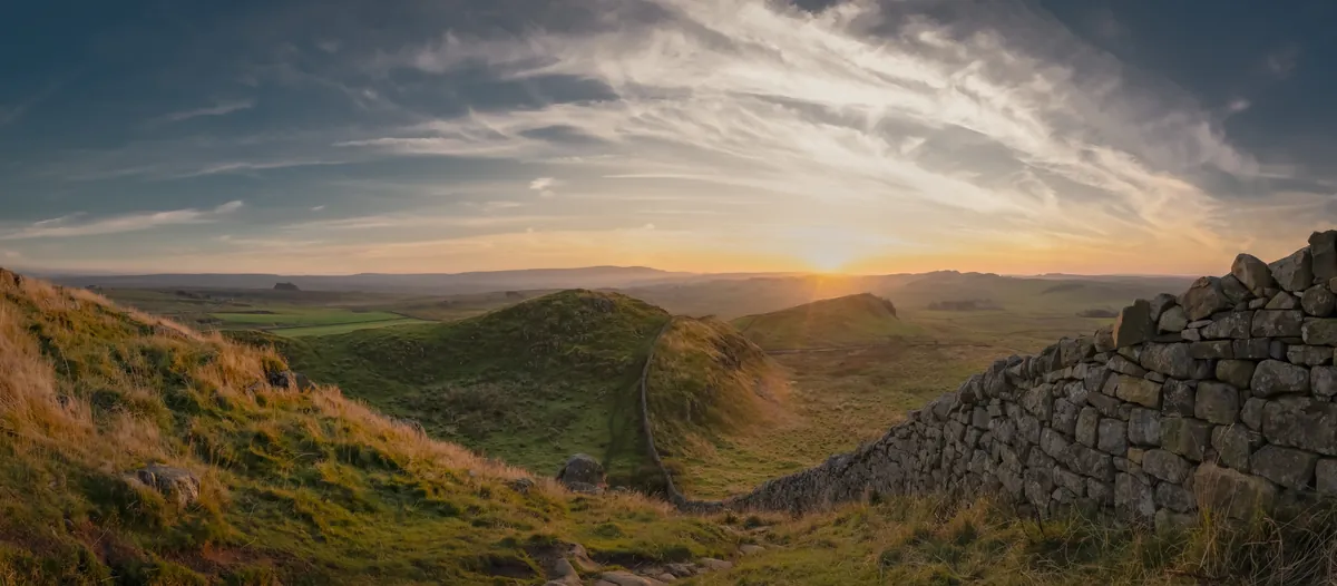 A wide view of the sun setting in gold along Hadrian's Wall