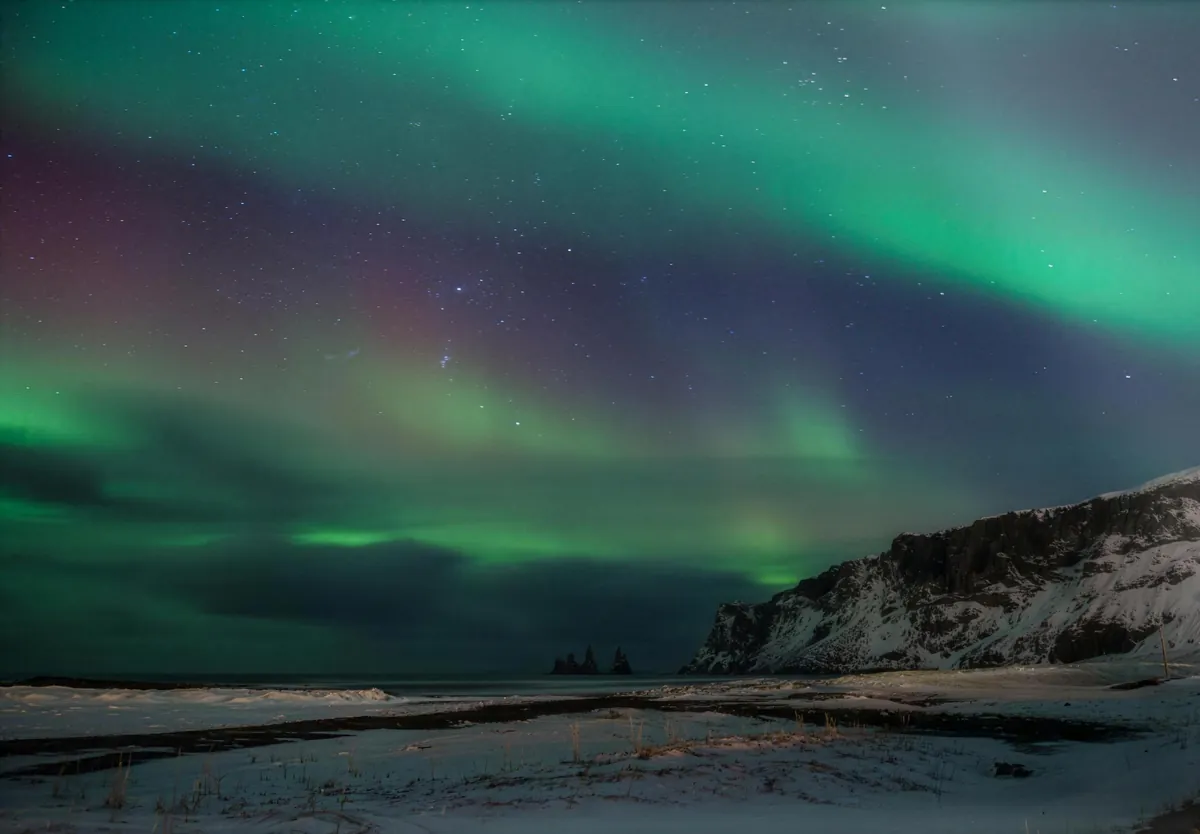 Green northern lights over the sea stacks and snowy cliffs at Vik, south Iceland