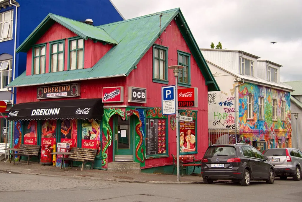 A red corner shop with a green roof and a painted mural on a street in Reykjavik