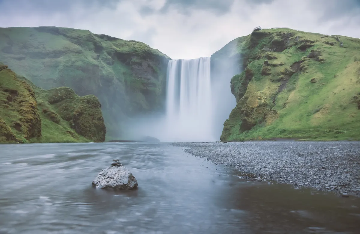 Skogafoss waterfall pouring between green cliffs into a wide river, Iceland